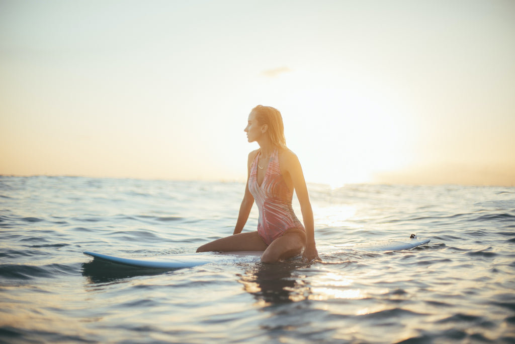Girl sitting on a surfboard during sunrise