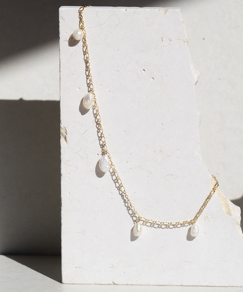sunlight shinning on stunning Thalassa necklaces on a marble stone